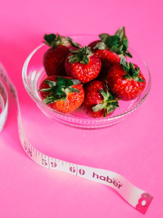 A glass bowl of fresh strawberries paired with a pink measuring tape symbolizes healthy eating.