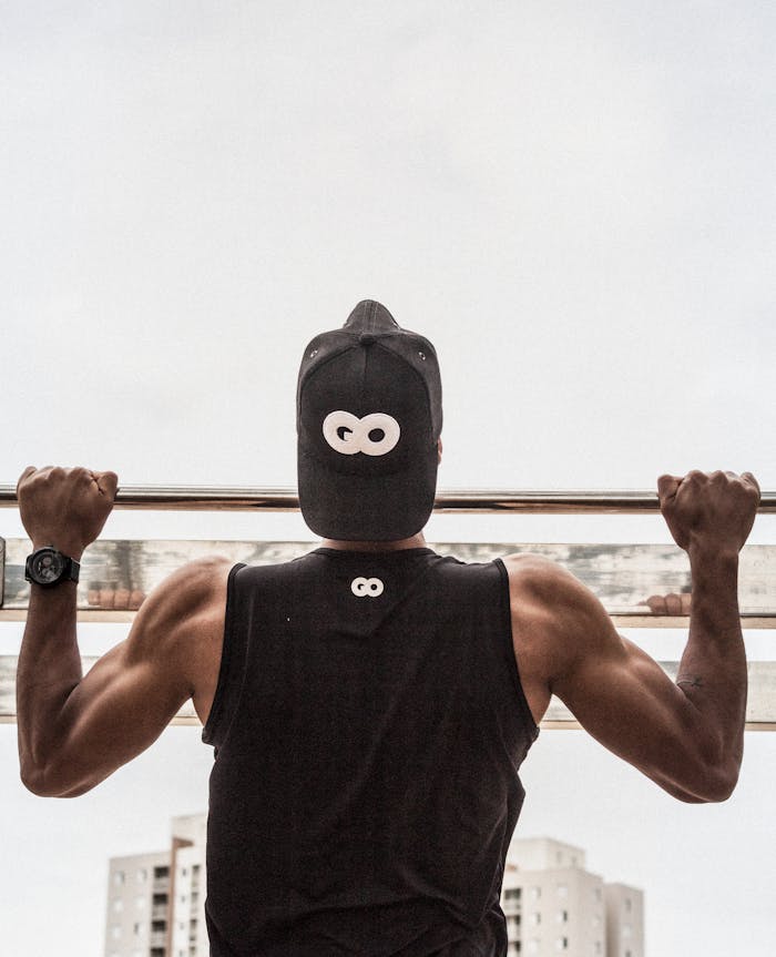 Back view of a man in gym attire doing pull-ups outdoors, demonstrating strength and fitness.