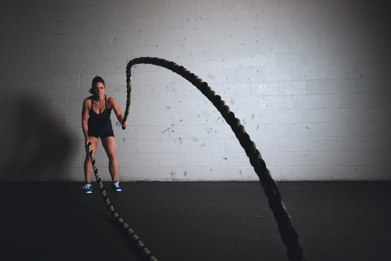 A focused woman performs a dynamic battle rope exercise in a gym setting, demonstrating strength and fitness.